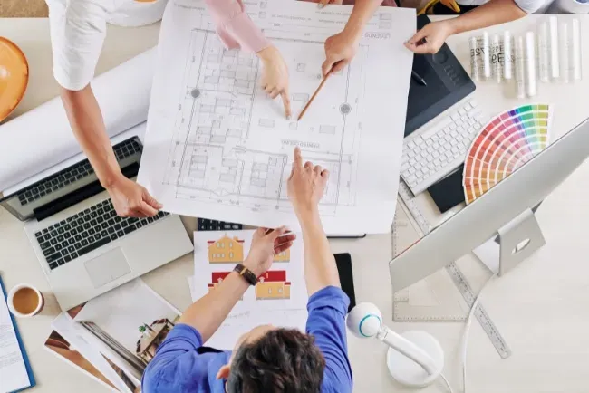 Collaboration among design build contractors while reviewing architectural plans on a workspace table